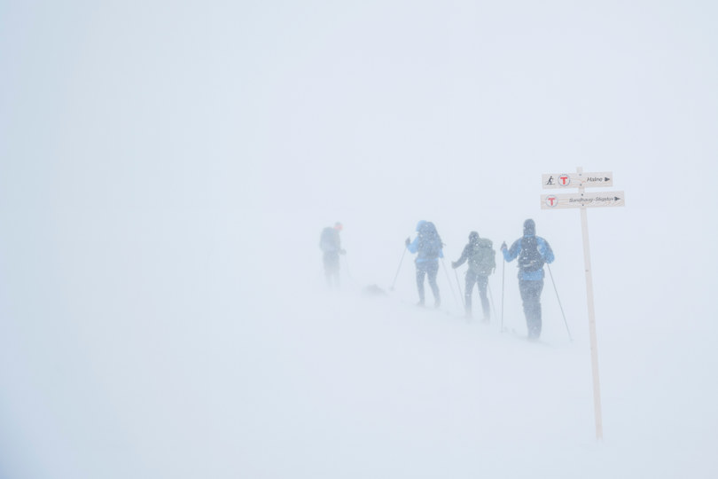 Fire skiløpere i tett tåke ved et skilt.