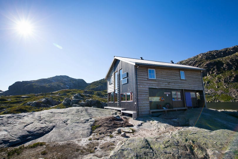 Grå plankekledd hytte i solskinn på høyfjellet.