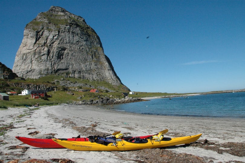 Gul og rød kajakk ligger på en sandstrand ved foten av et bratt fjell.