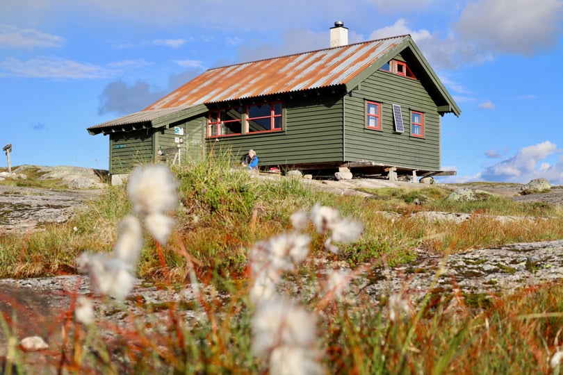 Person sitter utenfor ei grønn hytte på fjellet.