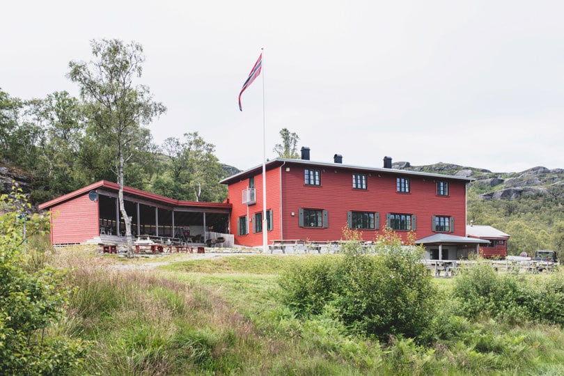 Stor rød hytte med flaggstang og vimpel på tunet.