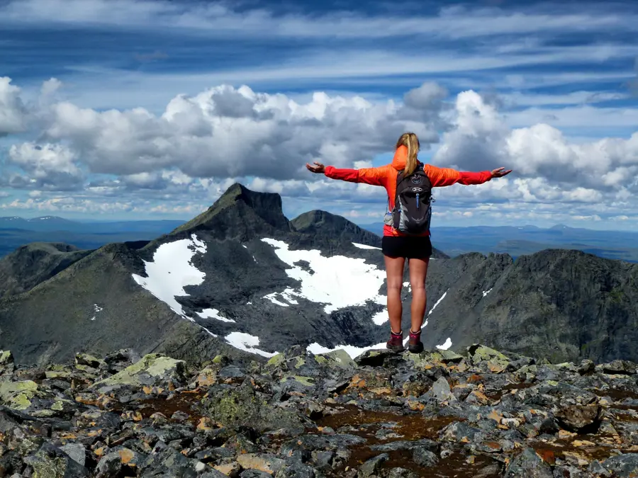 Person står med armene utstrakt og ser vekk fra oss, ut over steinete fjell-landskapet foran oss. 