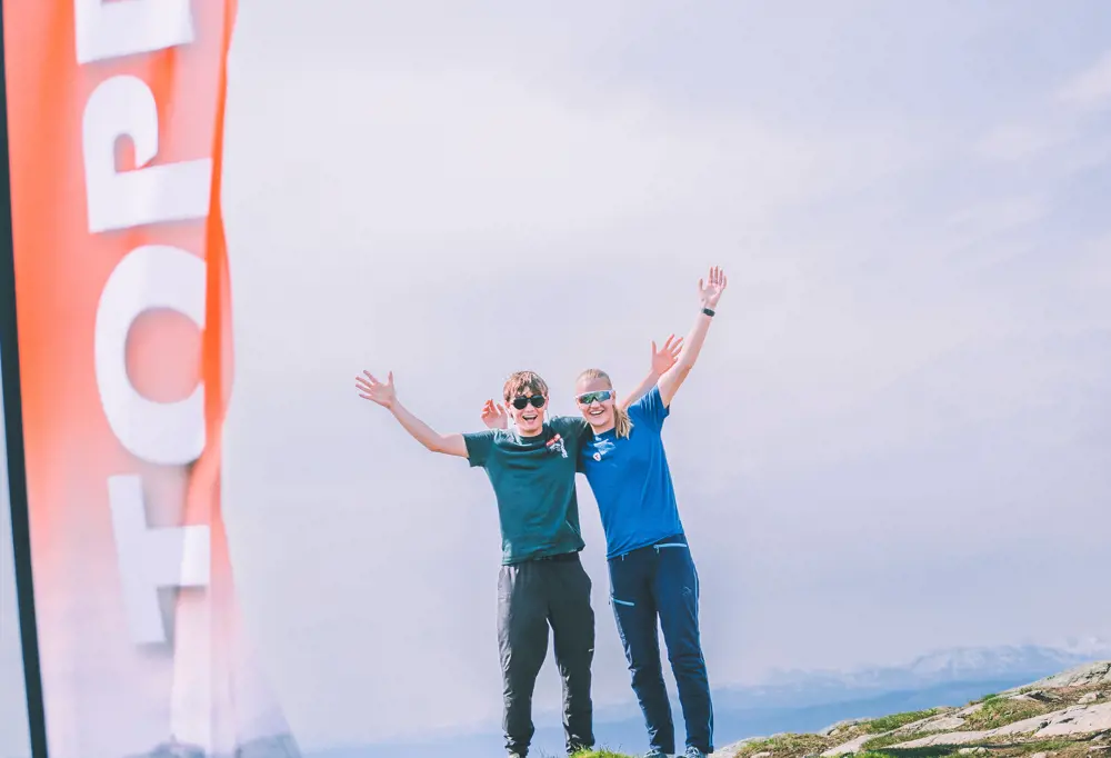 To menn på fjelltopp med armene i været 
