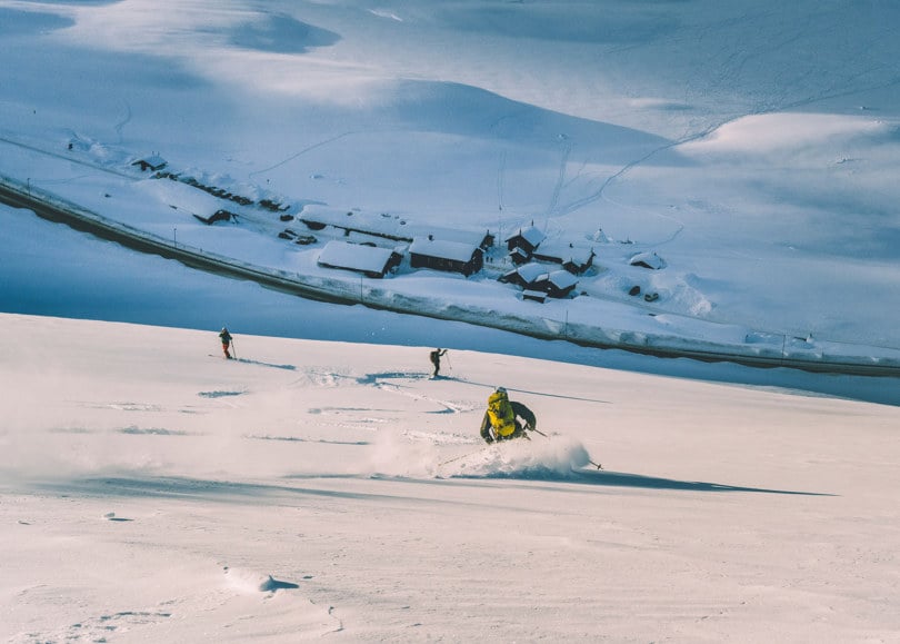 Tre skikjørere står på ski ned ei fjellside.