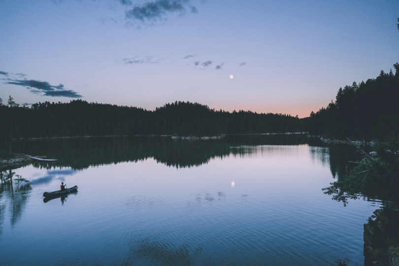 Person padler i kano i måneskinn på et stille skogsvann.