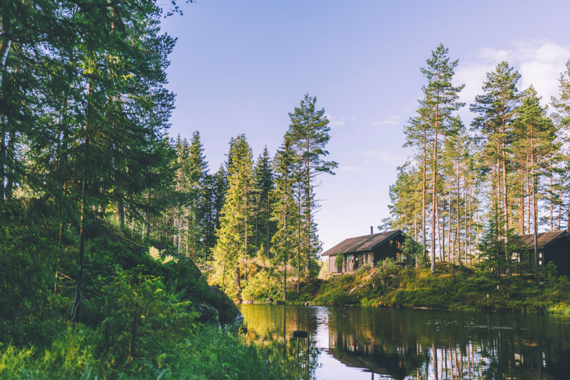Brun hytte på en liten odde ved et vann i skogen.