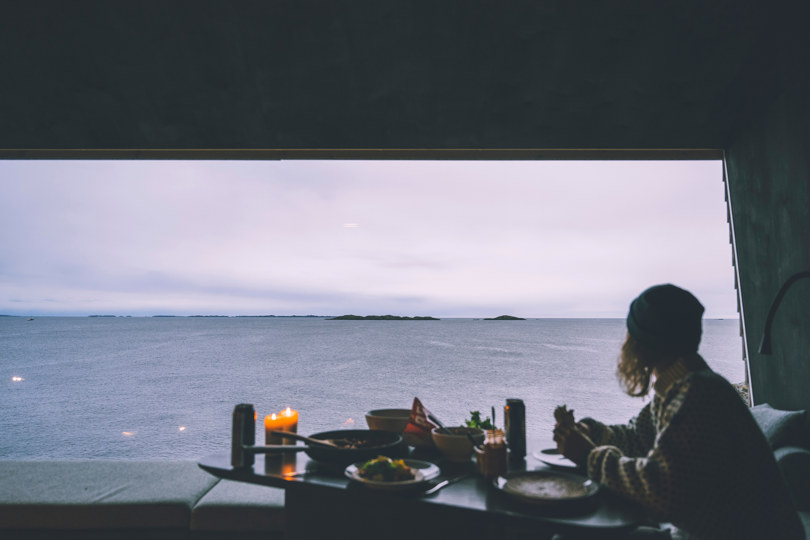 Silhuett av en person som spiser mat ved et stort vindu med utsikt over havet.