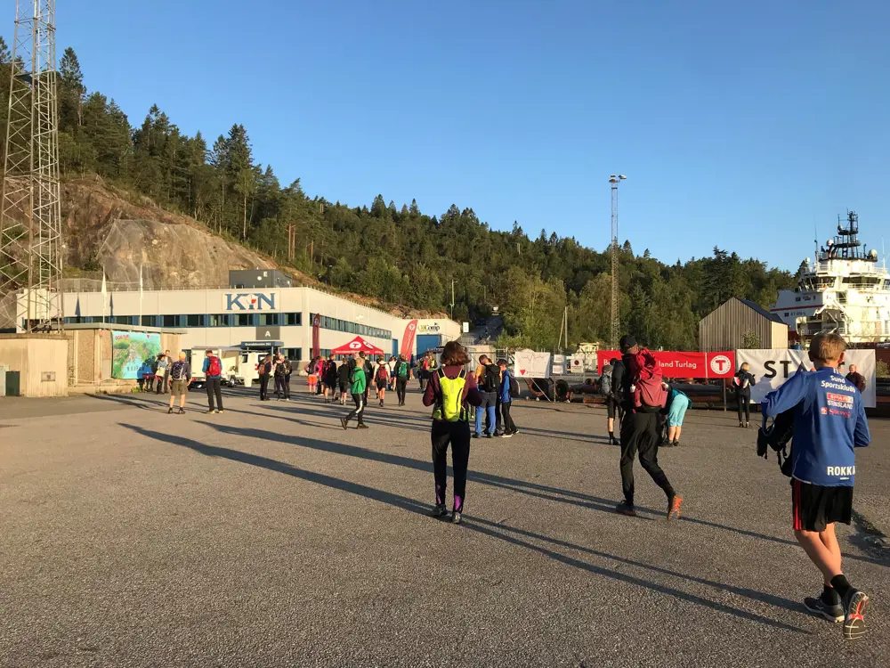 Folk går mot startområder på 7-fjellsturen en tidlig, solfylt morgenstund.