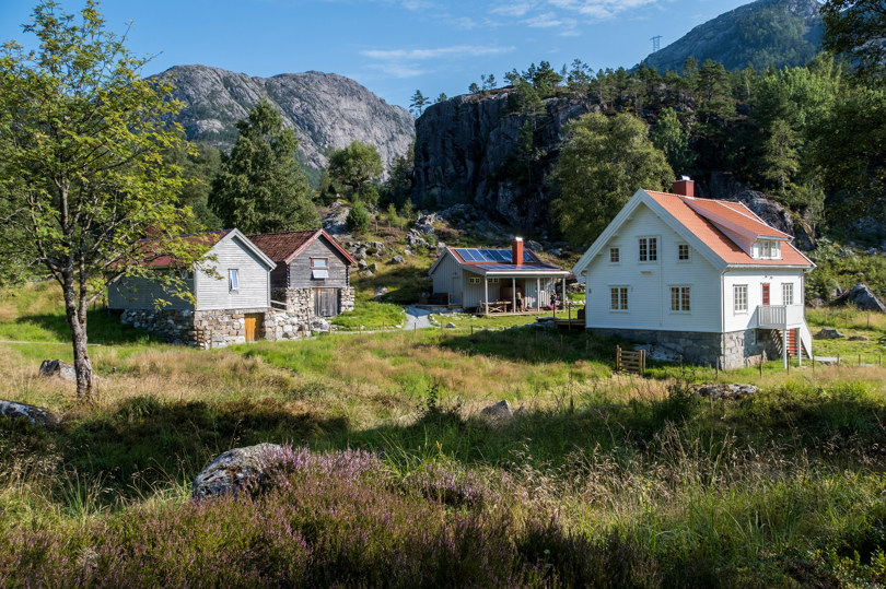 Fire gamle hus på steinmur rundt et tun med gress og eng.