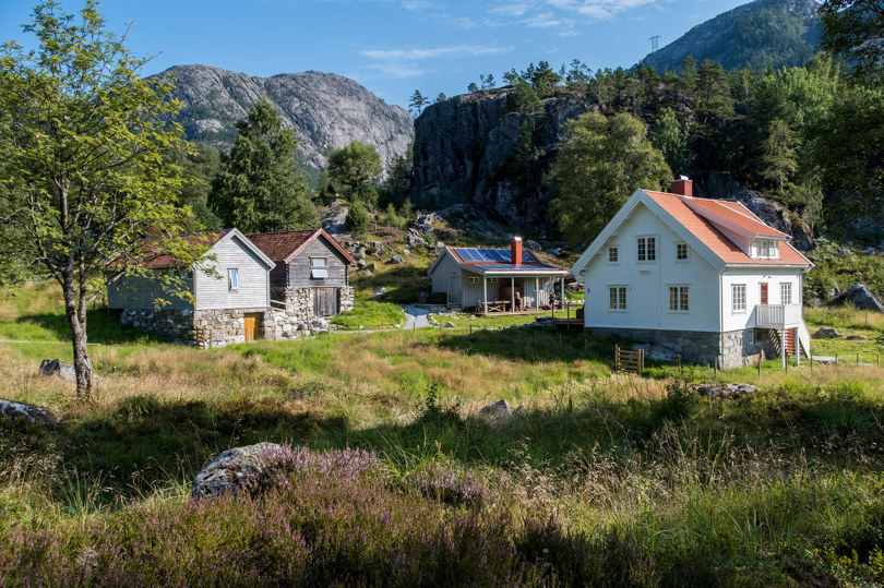 Fire gamle hus på steinmur rundt et tun med gress og eng. 