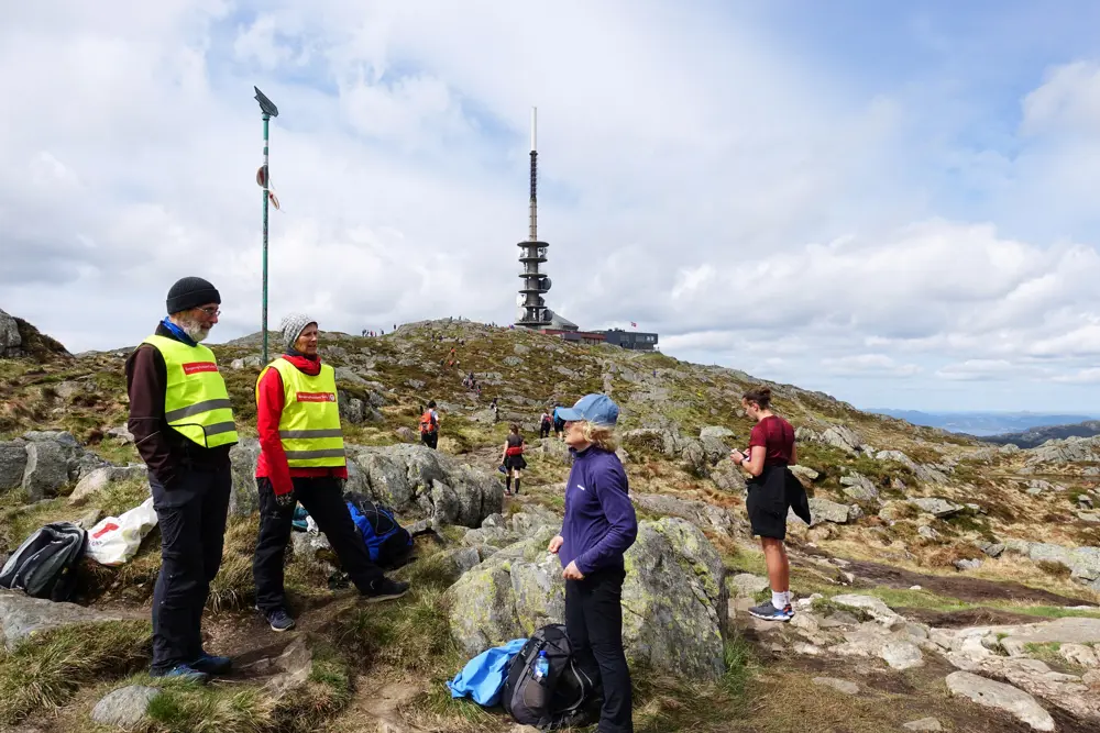 To friviilige står på en fjelltopp og tar i mot turgåere.