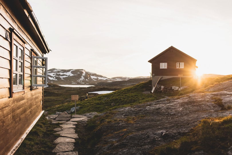 To hytter på fjellet. Sola går ned i bakgrunnen på den ene hytta.