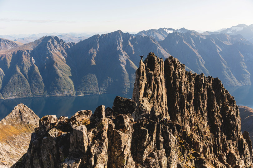 Person står på toppen av en fjellrygg med spisse tinder.