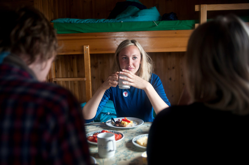 Kvinne i blå genser sitter ved et frokostdekket bord og drikker kaffe.