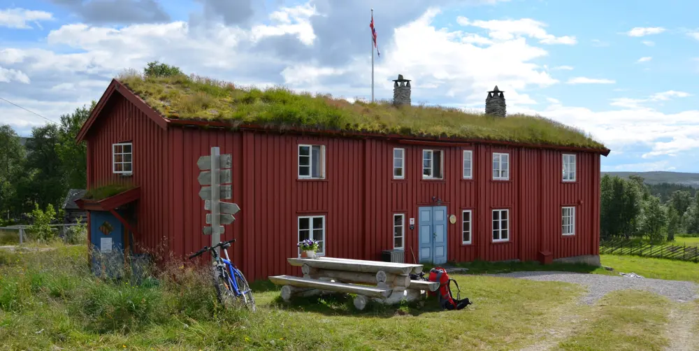 Blå himmel, grønt gress og rød hytte med torvtak 