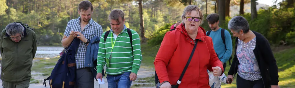 En liten gruppe mennesker går ved siden av hverandre langs et vann i skogen