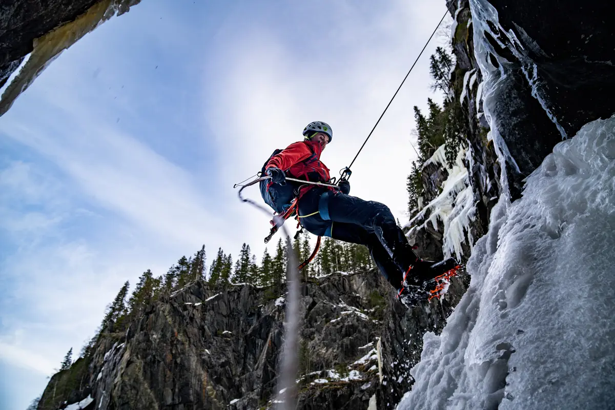 Mann som rappelerer ned på is i en bergvegg.