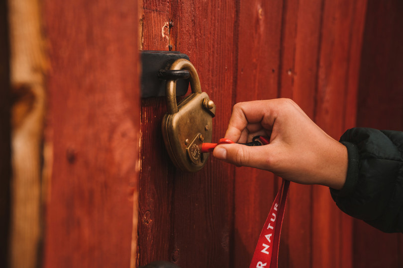 Bildet viser en stor hengelås på en dør, og en nøkkel er på vei å bli snudd i nøkkelhullet av en hånd.