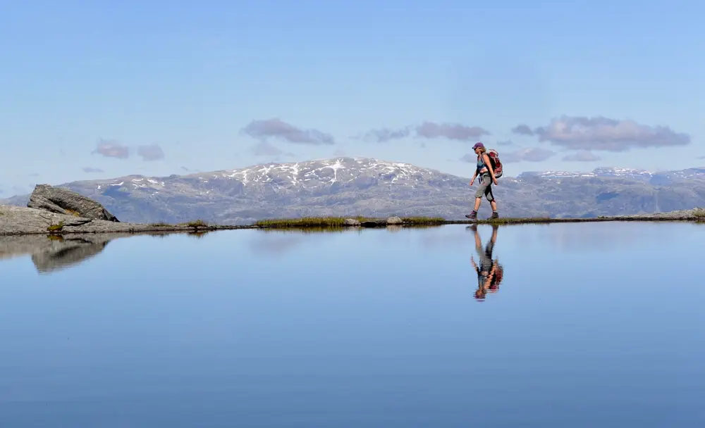 En kvinne som går på toppen av et feil ved siden av et vann. Speilbildet hennes vises i vannet.