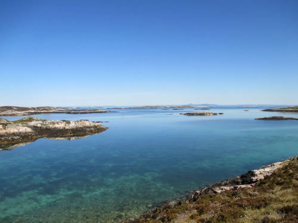 Utsikt over fjord eller innsjø, med noen få landbiter synlig til venste og i høyre hjørne, og videre ut i bakgrunnen. Skyfri himmel. 