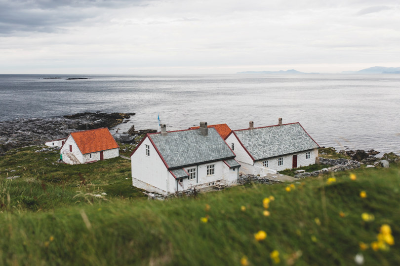 Fire små hvite hus på ei gresslette ved havet.