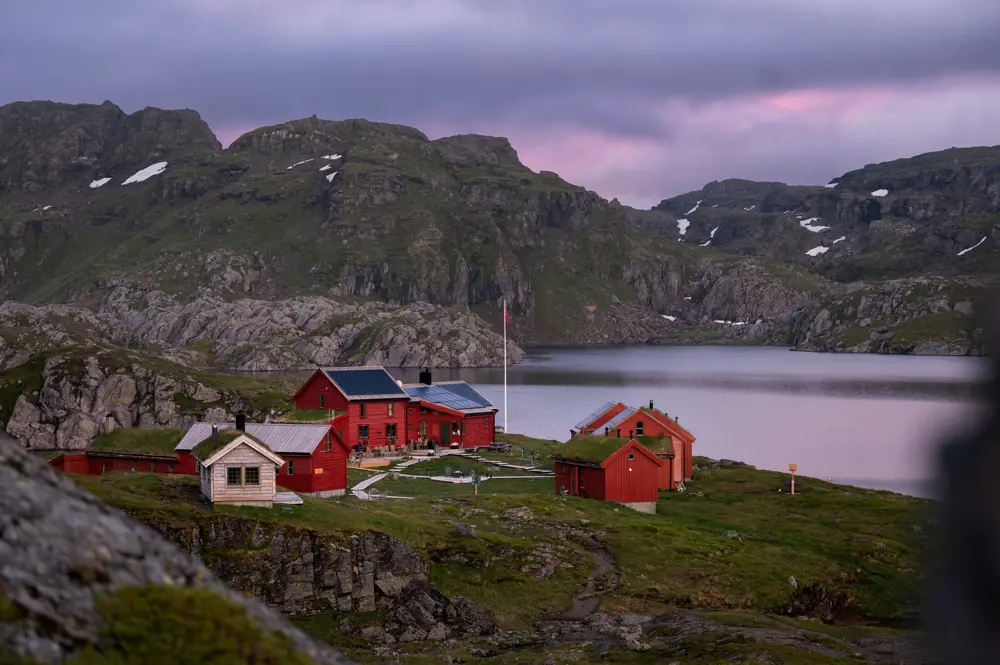 Røde hytter som ligger fint til ved et vann på fjellet.