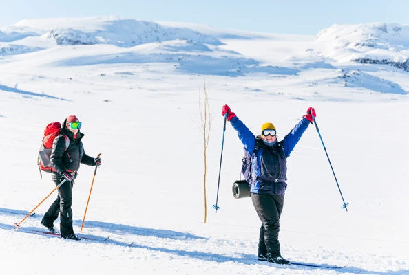 To skigåere i vinterfjellet, den ene holde armene opp i været