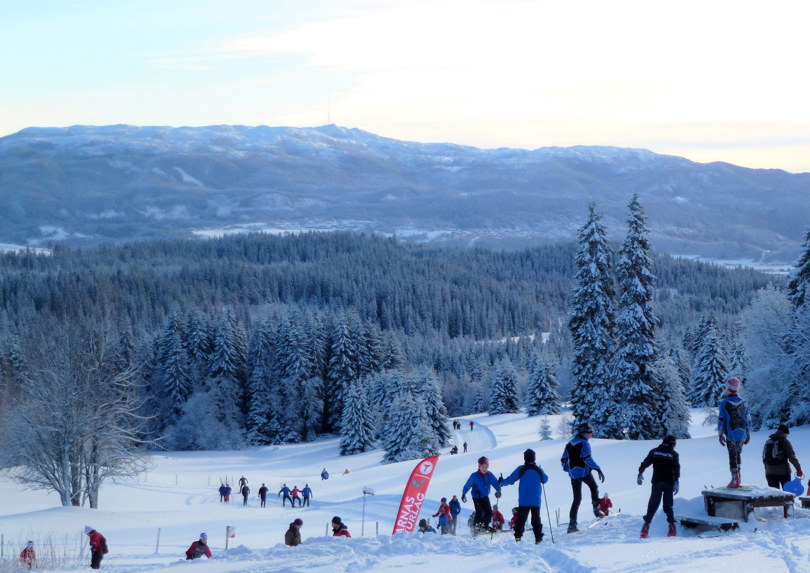 Masse mennesker og barn leker seg i skibakken med utsikt over marka.