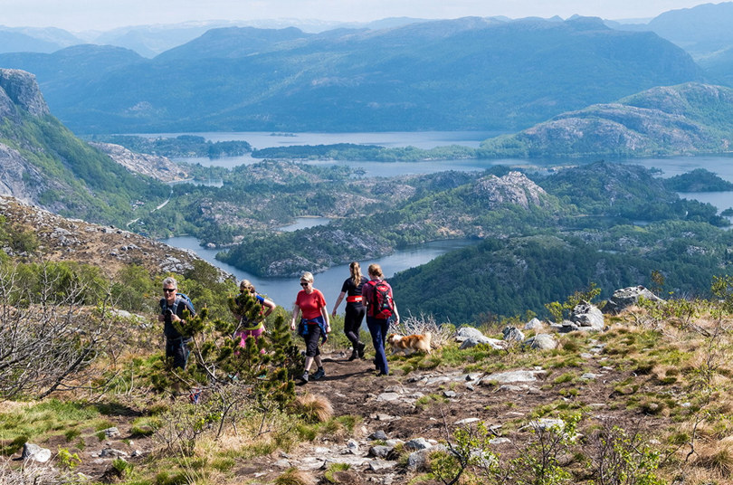 Utsikt fra toppen av Mattirudlå. Fjell, vann og grønt terreng. Mennesker som går opp og ned stien til fjelltoppen.