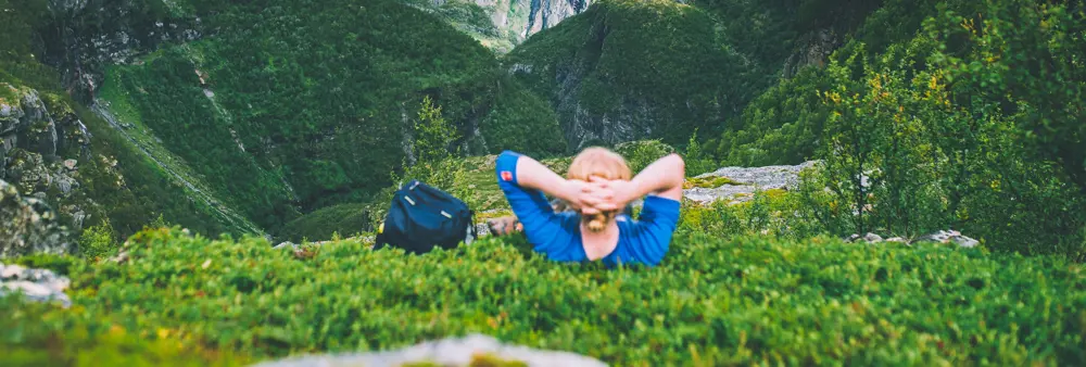 Mann som ligger i grønn lyng og ser utover fjell