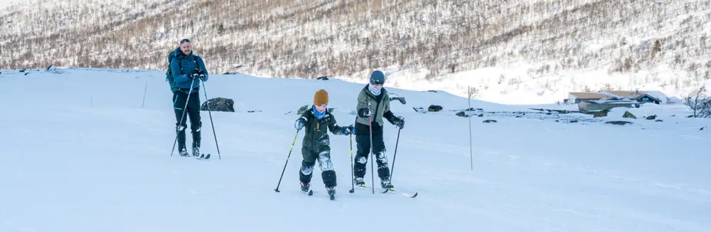 To barn og en voksen som går på ski i fjellet