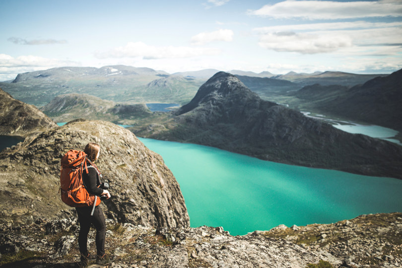 Dame som står på en fjelltopp og ser utover en blått fjellvann