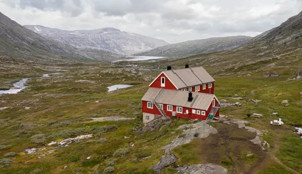 Stor, rødmalt hytte i fjellandskap.