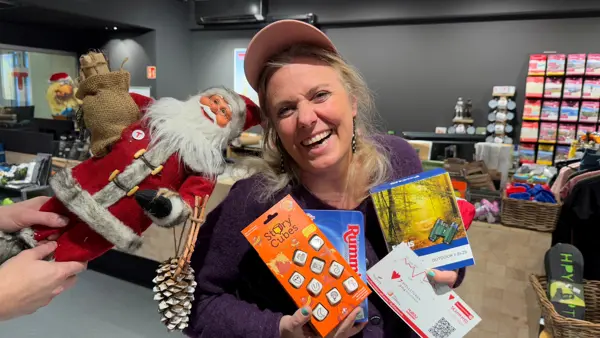 Smilende dame holder frem julegaver og en nisse kikker inn fra siden.