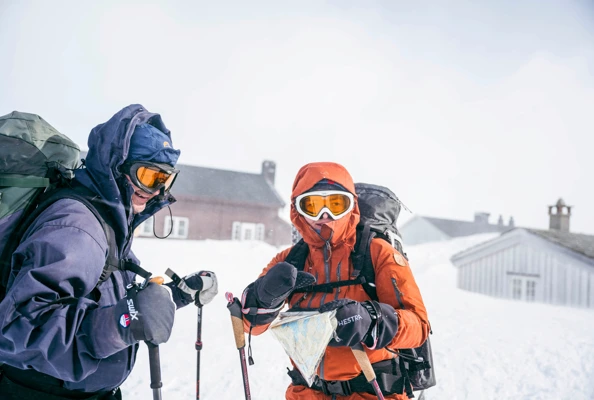 To skiløpere i vind i fjellet, med skibiller og hette.