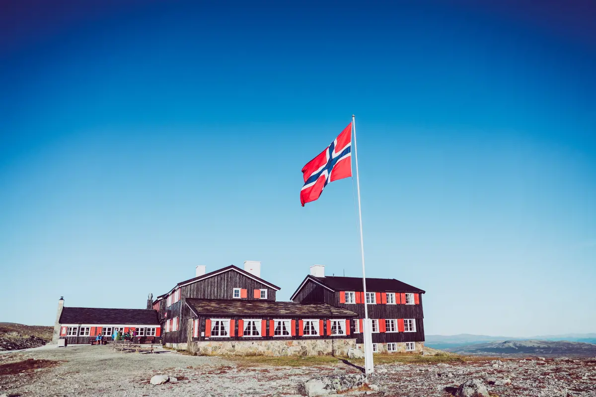 Svartmalt hytte med røde karmer og en flaggstang med en norsk flagg