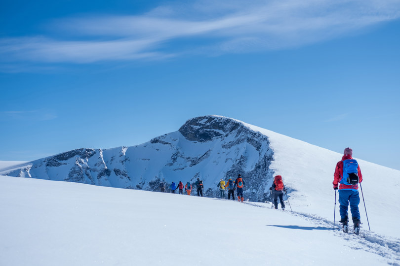 Flere personer som går på randonee ski over en fjelltopp