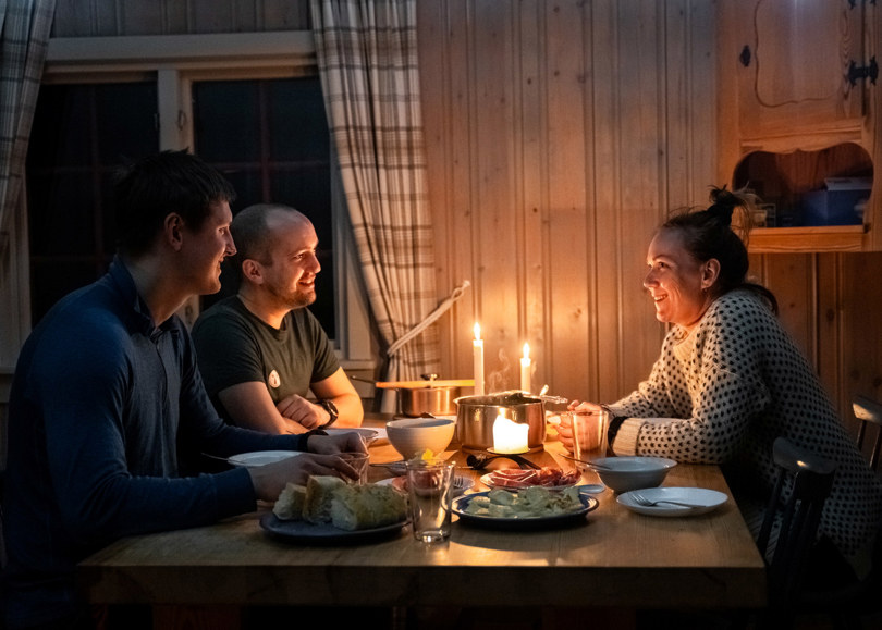 en gruppe mennesker som sitter rundt et bord med mat og stearinlys
