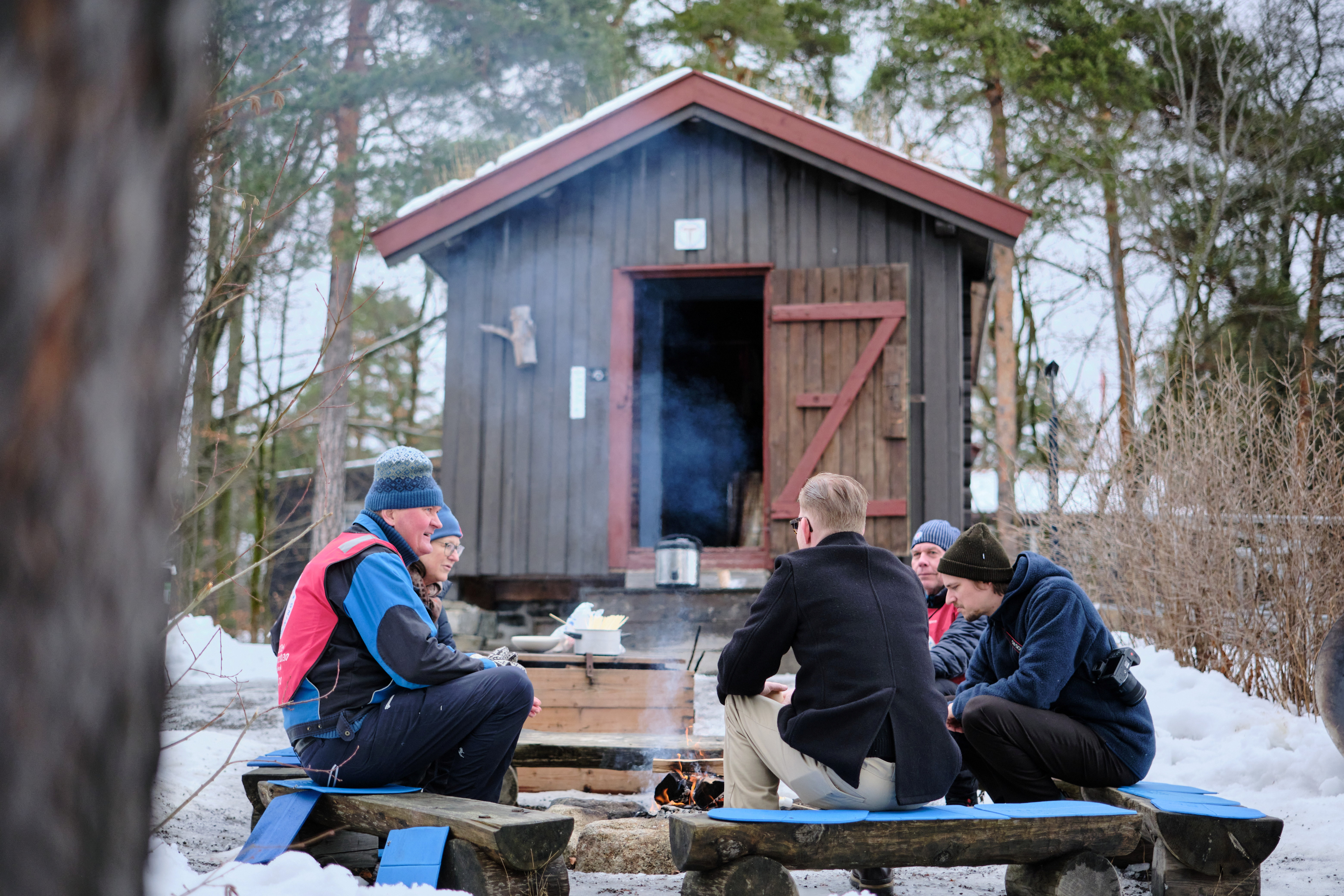 Flere personer som koser seg rundt bålet ved en hytte.