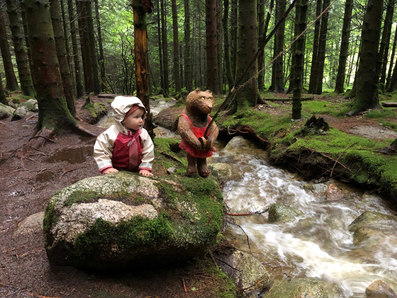 En liten jente og en utskjært trollfigur i en skog.