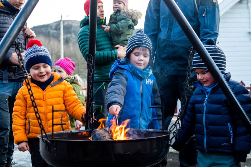 Fire gutter står ved en bålpanne og griller marshmallows.