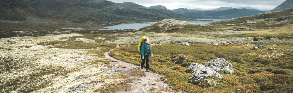 Dame med sekk på ryggen som går i fjellet