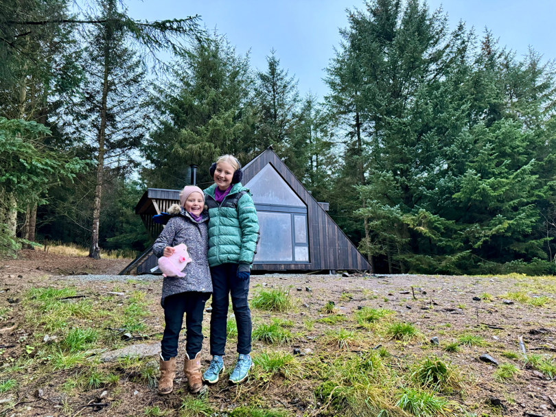 To barn står foran en brun liten hytte.