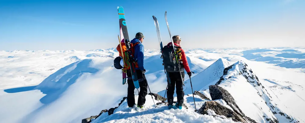 To personer med ski på sekken som ser utover fjellet
