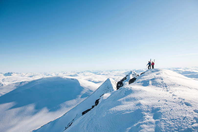 To personer som går over en fjellrygg med ski på sekken
