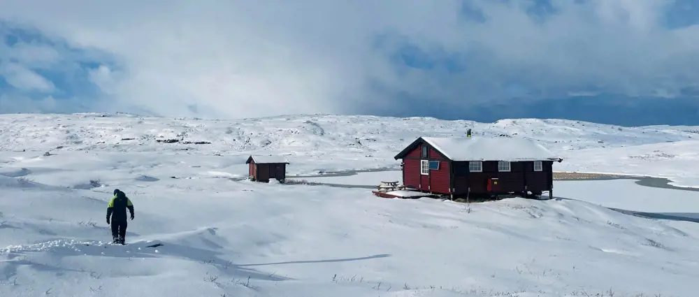 Rød hytte med vinterkledd fjellterreng. En person går innover mot hytta.