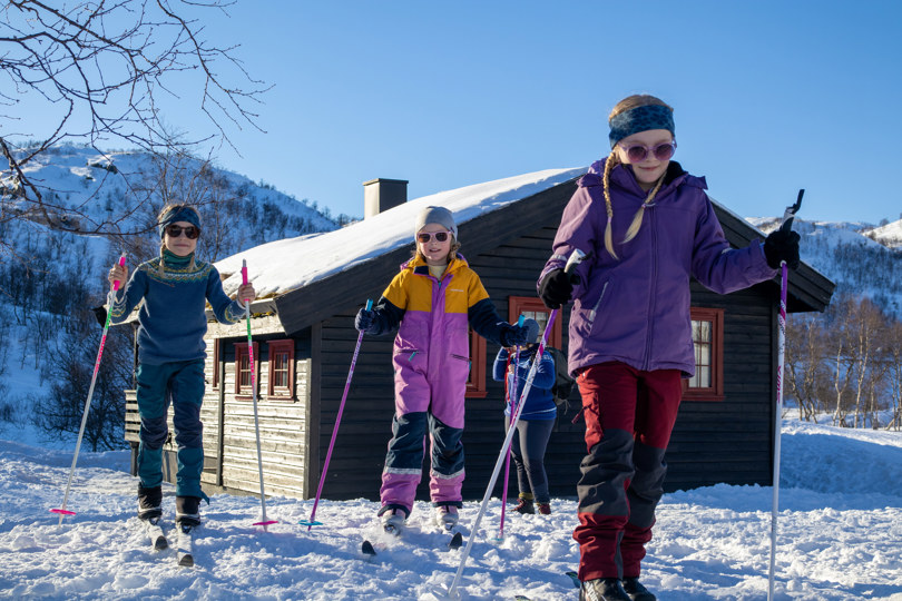 Fire barn går på ski ut fra en brun hytte.