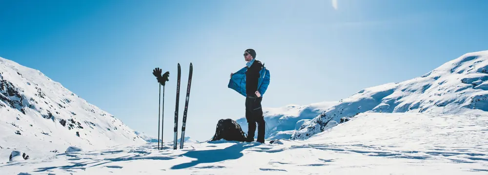 Mann som står i solen og tar av seg en jakke