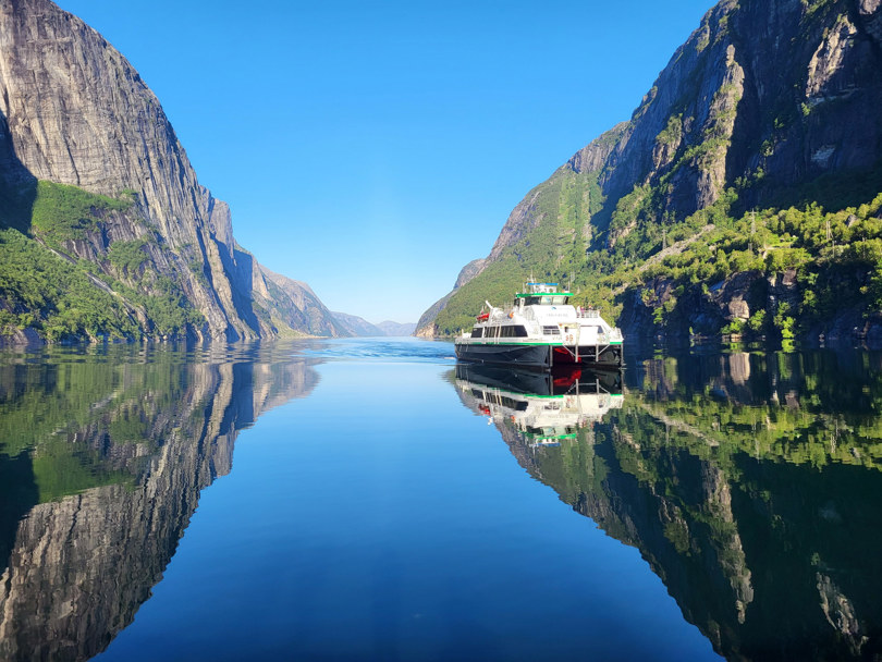 Båt på vei inn en speilblank fjord.