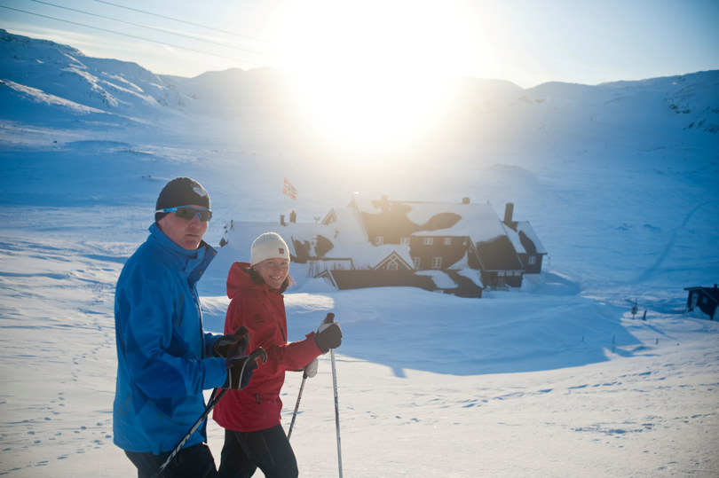 To skiløpere som står utenfor en svartmalt hytte